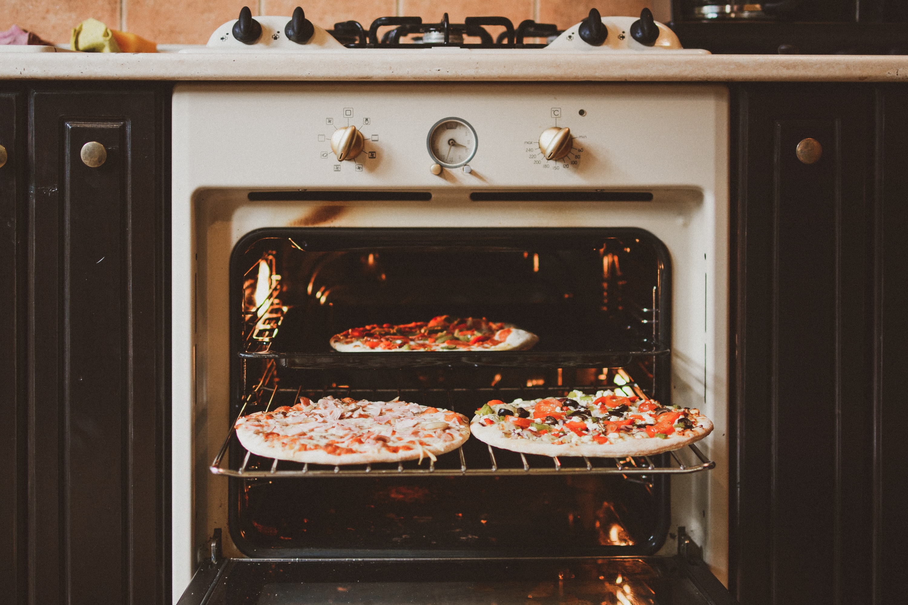 Photo of an open white oven with three furnished pizzas inside. Baking work does not end when you stick your food into the oven!